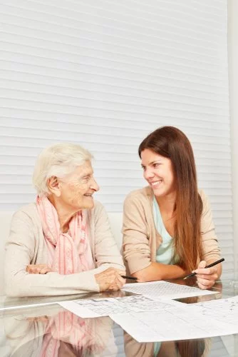 An elderly woman and a younger woman discuss documents at a table